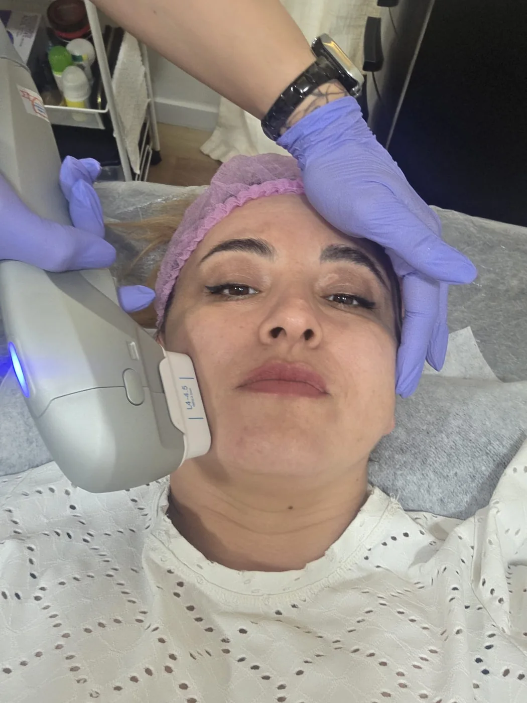 Cabezal de aparatología facial recorriendo el pómulo de una clienta en camilla